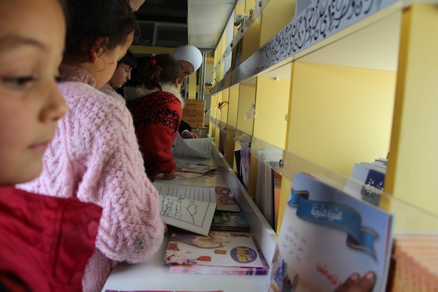 Displaced children choose their favourite stories inside the cultural bus in the Al-Azraq camp in northern Syria. Credit: Sonia Al Ali/IPS